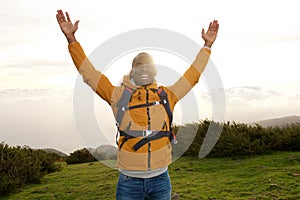 Happy african american backpacker standing outdoors with hands raised