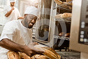 happy african american baker with tray of fresh loaves of bread