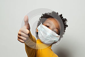 Happy African American black kid in medical protective face mask showing thumb up on white photo