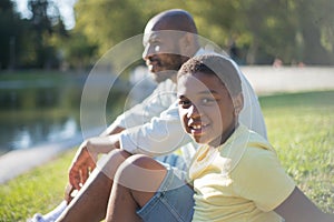 Happy African American boy sitting on lake shore with his dad