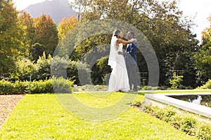 Happy african american bride and groom embracing at wedding in sunny garden, copy space