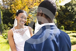 Happy african american bride and groom smiling at wedding ceremony in sunny garden