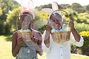 Happy african american brother and sister in bunny ears holding baskets of easter eggs