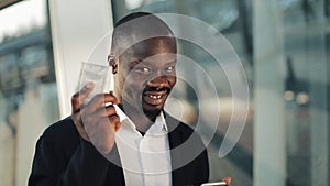 Happy african american businessman cheering celebrating looking at cell phone and holding a big amount of money in his