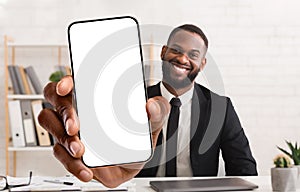 Happy african american businessman showing cellphone with big blank screen at office, mockup for app or website design