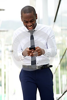 Happy african american businessman walking and looking at cellphone on city street