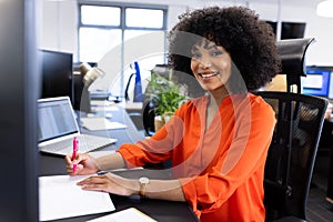 Happy african american businesswoman sitting at desk and smiling at camera