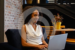 Happy african american casual businesswoman using laptop in office lounge