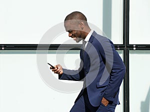 Happy african american corporate businessman walking with cellphone in city