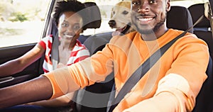 Happy african american couple in car with their pet dog on backseat