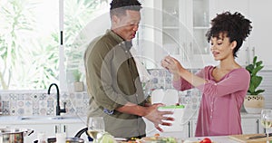 Happy african american couple cooking and dumping waste in kitchen