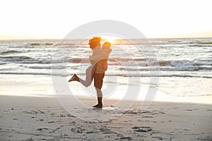 Happy african american couple embracing on beach by sea at sunset