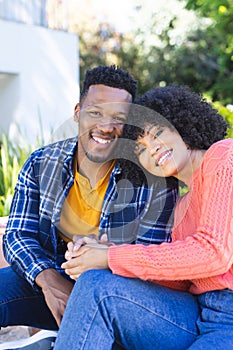 Happy african american couple embracing and holding hands on stairs in sunny garden, copy space