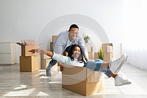 Happy african american couple having fun and fooling while moving to new home. Joyful woman riding in cardboard box