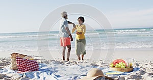 Happy african american couple having picnic and dancing on sunny beach