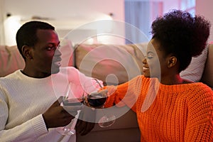 Happy african american couple in love man and woman drink red wine, enjoy romantic date at home
