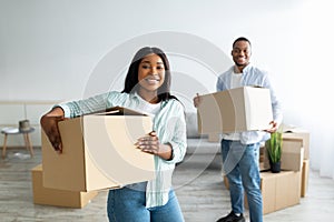 Happy african american couple moving house, holding paper boxes and unpacking them after relocating to own accommodation