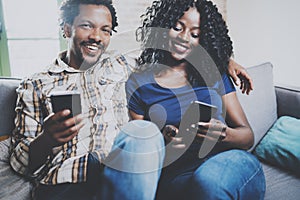 Happy african american couple relaxing together on the sofa.Young black man and his girlfriend using mobile phones while