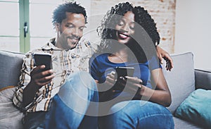 Happy african american couple relaxing together on the sofa.Young black man and his girlfriend using smartphones while