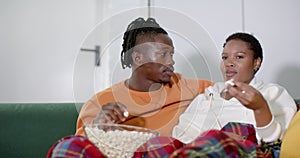 Happy african american couple relaxing watching tv and eating popcorn at home, slow motion