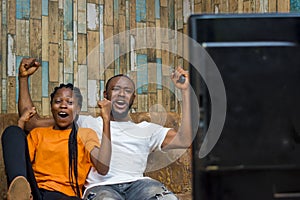 Happy African american couple sitting and cheering while watching television