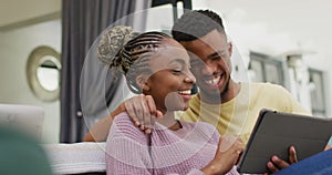 Happy african american couple sitting on sofa and relaxing with tablet