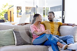 Happy african american couple smiling and embracing on couch in sunny living room