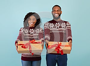 Happy african american couple stretching Christmas gifts to camera over blue studio background, celebrating New Year