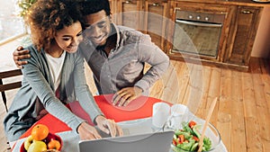 Happy african-american couple using laptop at kitchen