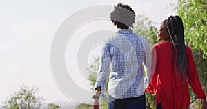 Happy african american couple walking together and holding hands on sunny day, slow motion