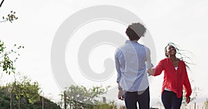 Happy african american couple walking together and holding hands on sunny day, slow motion