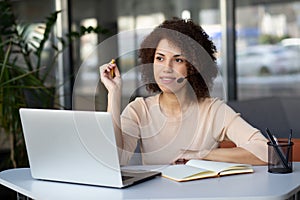 Happy african american curly haired young woman with headset, help desk worker, call center operator, consultant, talking with