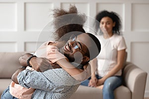 Happy african american dad embracing daughter cuddling at home