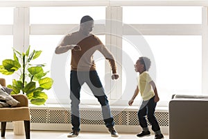 Happy african dad and toddler son dancing in living room