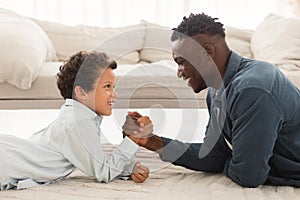 Happy African American Daddy And Little Son Arm Wrestling Indoor