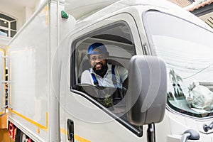 Happy African American delivery service man driver in uniform sitting smiling and looking on camera cheerful in a courier truck