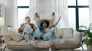 Happy African American ethnic couple jumping on sofa laugh having fun fooling around enjoy relax rest fall on cozy couch