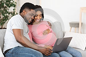 Happy african american expecting family using laptop at living room
