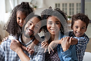 Happy African American family couple piggybacking two kids at home