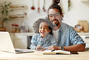 Happy african american family father and son sitting at table with laptop during distance education