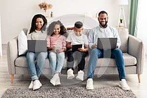 Happy african american family holding and using personal gadgets