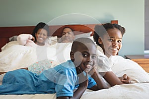 Happy African American family looking at camera while relaxing on bed in bedroom