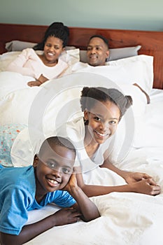 Happy African American family looking at camera while relaxing on bed in bedroom