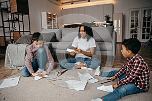 Happy African american family, mother and two sons having fun time at home and fly paper airplanes