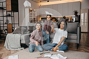 Happy African american family, mother and two sons having fun time at home and fly paper airplanes