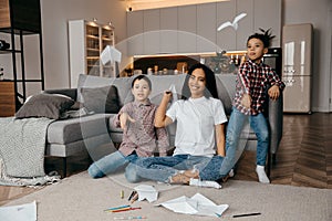 Happy African american family, mother and two sons having fun time at home and fly paper airplanes photo