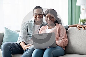 Happy african american family sitting on couch, using laptop