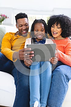 Happy african american family sitting on couch and using tablet at home, copy space