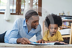 Happy African American family spending time together at home. Cute black son and his handsome father are reading a book while