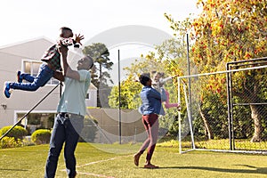 Happy african american family spending time together and playing football outside